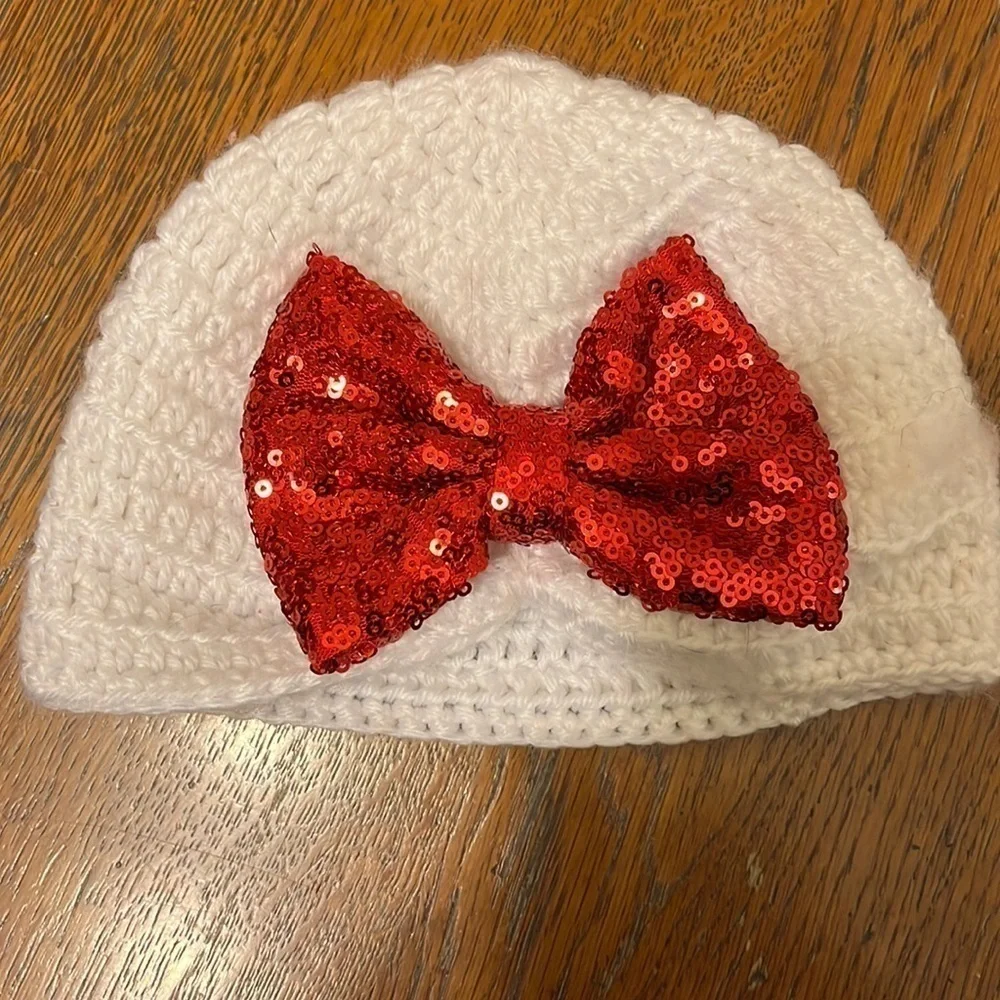 White crocheted hat with red glitter bow. Infant size 6-12mo.